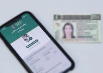 Celular exibindo o aplicativo e-Título com a mensagem "Biometria coletada" ao lado de uma carteira de identidade