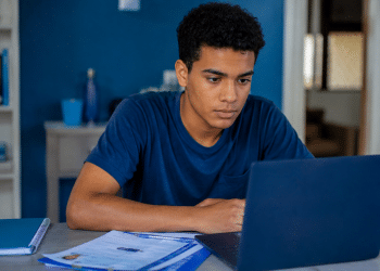 Estudante jovem utilizando notebook e materiais de estudo em casa durante preparação para o Enem.
