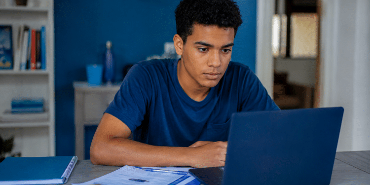 Estudante jovem utilizando notebook e materiais de estudo em casa durante preparação para o Enem.