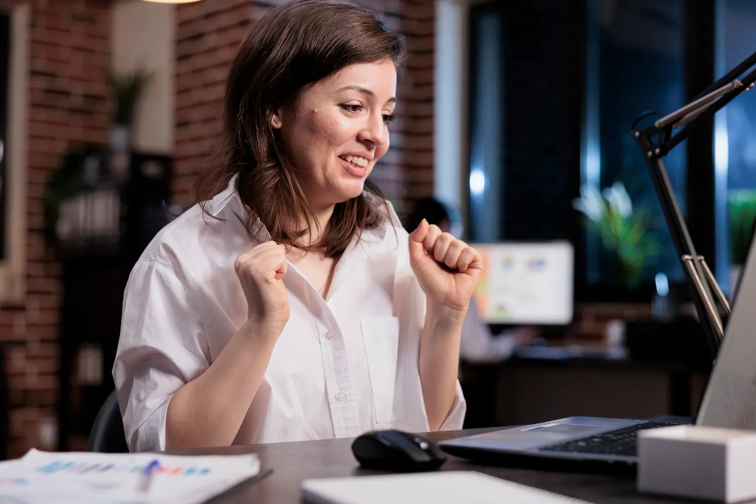 Mulher sorrindo e comemorando conquistas pessoais em ambiente de trabalho, simbolizando fortalecimento da autoconfiança.