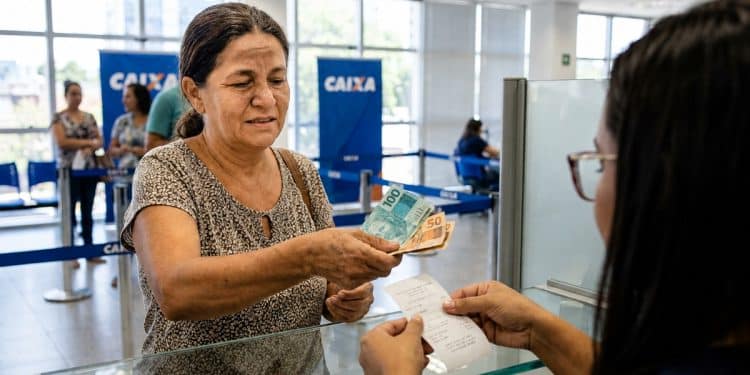 Mulher saca notas de R$ 100 e R$ 50 no caixa de uma agência da Caixa, em imagem que ilustra os pagamentos do Bolsa Família de junho, iniciados no dia 17 e mantidos até o dia 30