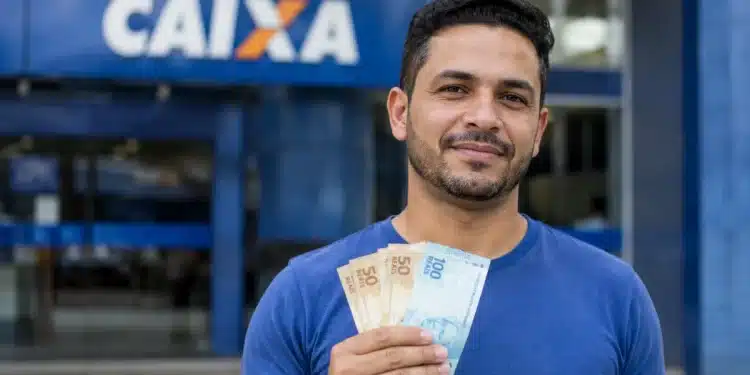 Homem brasileiro em frente à agência da Caixa Econômica Federal segurando dinheiro, representando liberação de saque de até R$ 6.220.