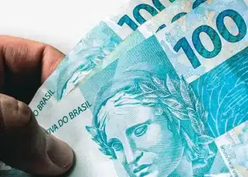 Notas de R$ 100 reais sendo seguradas em destaque, representando a liberação do Caixa Tem no valor de R$ 200.