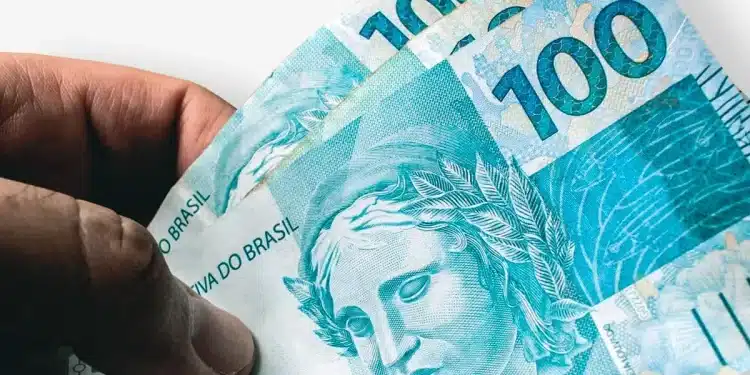 Notas de R$ 100 reais sendo seguradas em destaque, representando a liberação do Caixa Tem no valor de R$ 200.