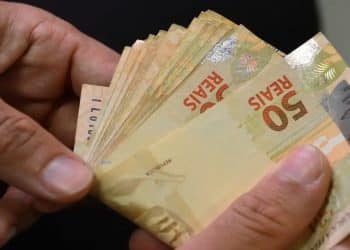 Mãos contando cédulas de R$ 50, representando o pagamento de R$ 2.216 que une o abono salarial e o Cashback do Imposto de Renda em 15 de julho.