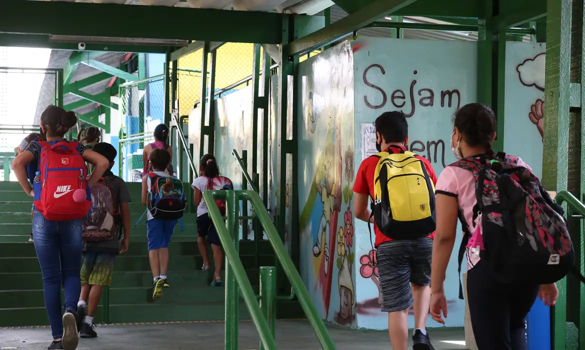 Crianças com mochilas escolares entrando em escola pública, representando o direito à educação inclusiva para alunos com dislexia e TDAH