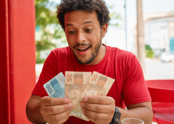 Homem sorri surpreso ao contar notas de cem e cinquenta reais em ambiente externo
