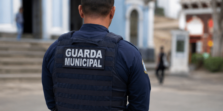 Guarda municipal visto de costas usando uniforme em área urbana.