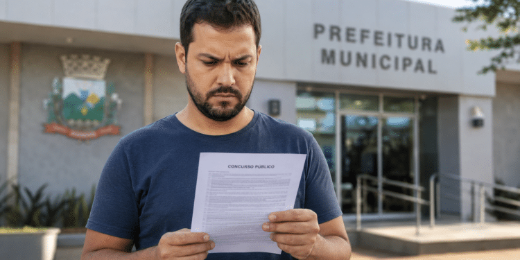 Homem lendo edital de concurso público em frente à Prefeitura Municipal.