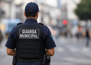 Guarda municipal visto de costas durante patrulhamento em área urbana com fundo desfocado.