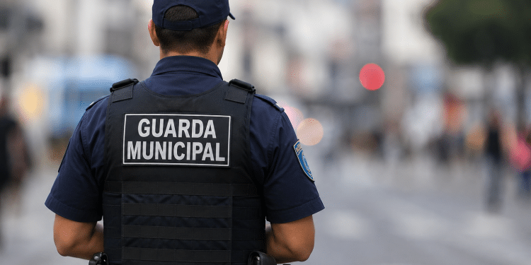 Guarda municipal visto de costas durante patrulhamento em área urbana com fundo desfocado.