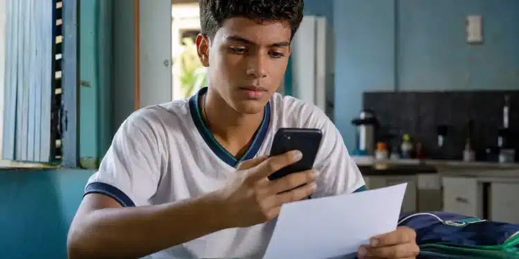 Estudante brasileiro segurando um documento e um celular em casa, representando o processo de confirmação da inscrição no Enem 2026 para candidatos isentos.