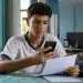 Estudante brasileiro segurando um documento e um celular em casa, representando o processo de confirmação da inscrição no Enem 2026 para candidatos isentos.