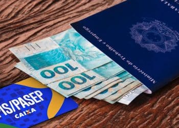 Carteira de Trabalho azul ao lado de cédulas de R$ 100 e cartão PIS/PASEP da Caixa, representando a consulta do Abono Salarial do quinto grupo