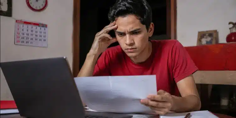 Jovem estudante brasileiro concentrado em notebook, em ambiente doméstico simples, com expressão de atenção e preocupação, representando a inscrição no Enem 2026 antes do prazo final.