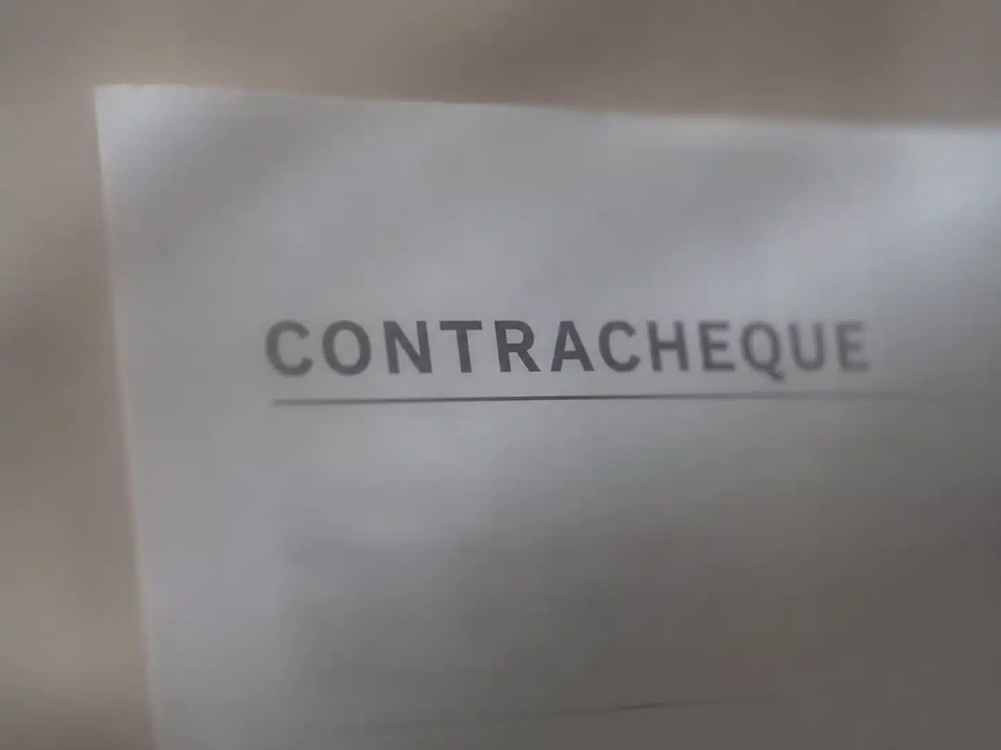 Documento desfocado com a palavra “contracheque” escrita sem hífen, destacando a grafia correta segundo a ortografia atual.