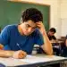 Estudante concentrado escrevendo a redação, demonstrando foco e leve tensão, representando as regras de correção da redação do Enem.