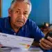 Idoso segurando extrato do INSS e celular em casa, com expressão de preocupação, representando os cuidados necessários para não perder o benefício do INSS.