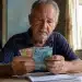 Idoso do INSS segurando cédulas de dinheiro, representando o depósito de R$ 2.431,50 ou valor menor para esta terça-feira, 2 de junho.
