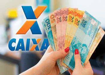 Mão feminina com unhas vermelhas segurando notas de R$ 50, R$ 10, R$ 20 e R$ 100 ao lado do logo da Caixa, simbolizando o último desbloqueio do valor de R$ 1.000 em 2026.