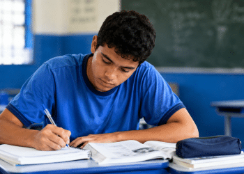 Estudante brasileiro escrevendo redação à mão durante estudo para o Enem em sala de aula.
