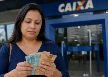 Mulher conferindo cédulas de dinheiro em frente à agência da Caixa, com dúvidas sobre a elegibilidade ao PIS/Pasep para quem recebe R$ 3.000.