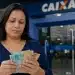Mulher conferindo cédulas de dinheiro em frente à agência da Caixa, com dúvidas sobre a elegibilidade ao PIS/Pasep para quem recebe R$ 3.000.