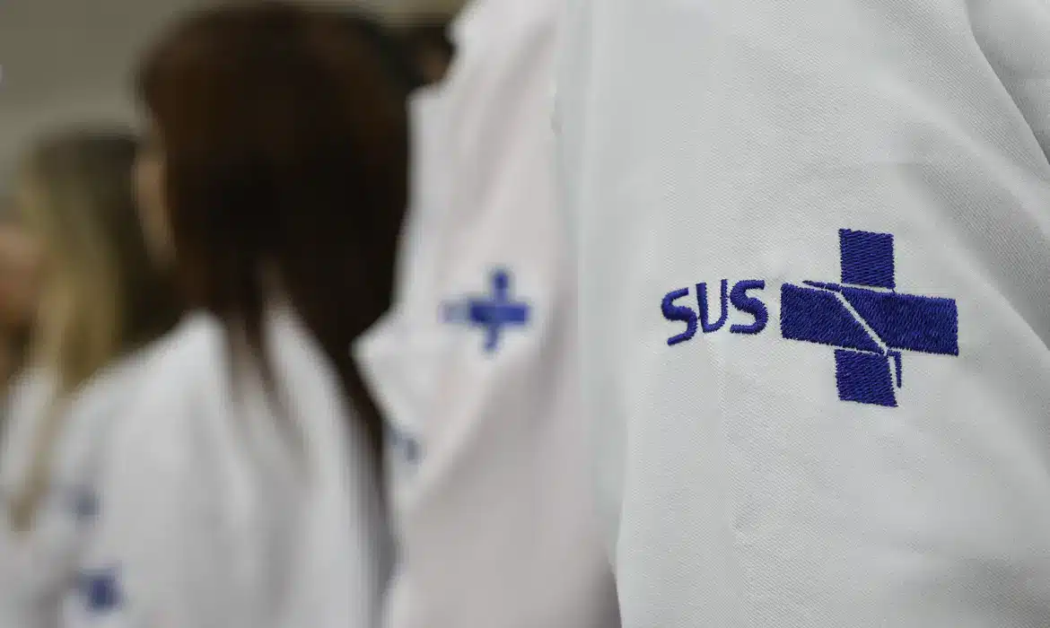 Profissionais de jaleco branco com o símbolo do SUS bordado na manga, em imagem que ilustra a avaliação da formação médica feita pelo Enamed 2026