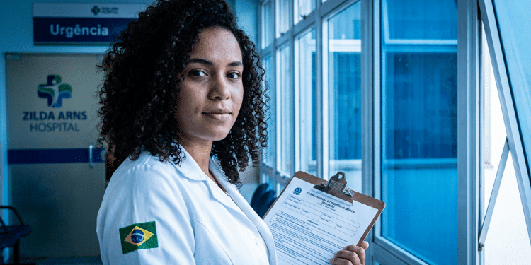 Médica de jaleco segura formulário do Exame Nacional de Residência em hospital, representando as mudanças do Enare 2026/2027