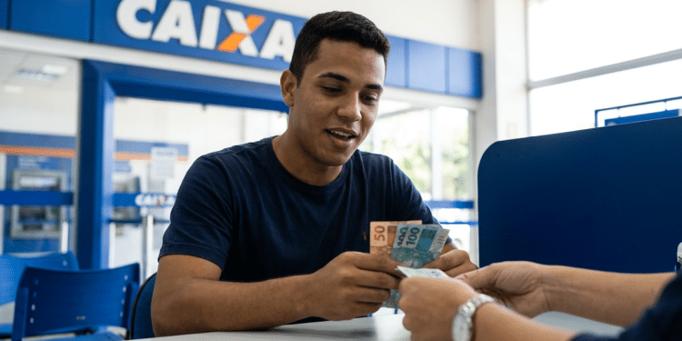 ovem recebe cédulas de real no caixa de uma agência da Caixa