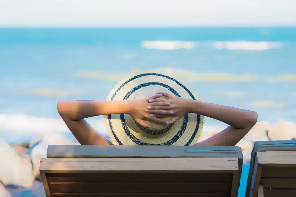 Mulher relaxando em espreguiçadeira à beira-mar, representando descanso e planejamento dos feriados nacionais restantes de 2026 no Brasil
