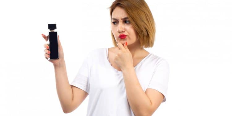 Mulher de camiseta branca observa frasco de perfume preto com expressão de dúvida