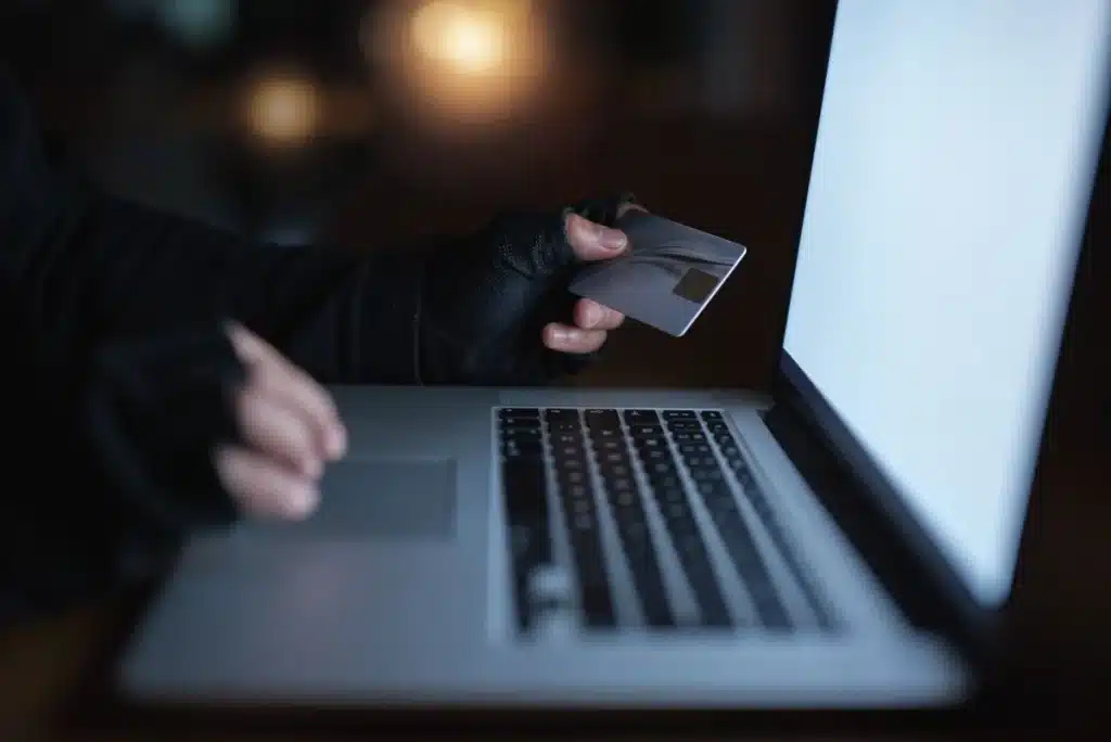 Pessoa com cartão de crédito em frente ao notebook evidenciando golpes com aplicativo falso de reembolso do INSS