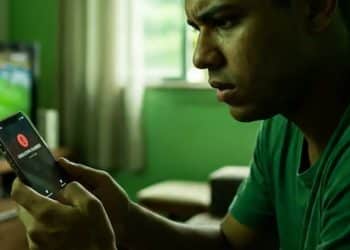 Homem acompanha jogo de futebol enquanto recebe alerta de possível golpe no celular.