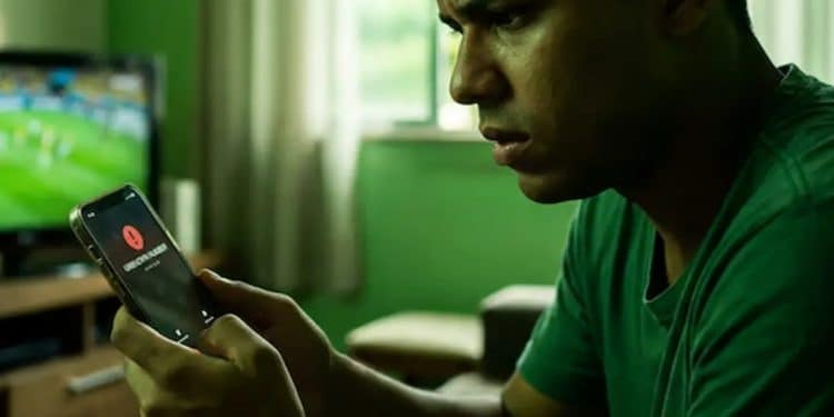 Homem acompanha jogo de futebol enquanto recebe alerta de possível golpe no celular.