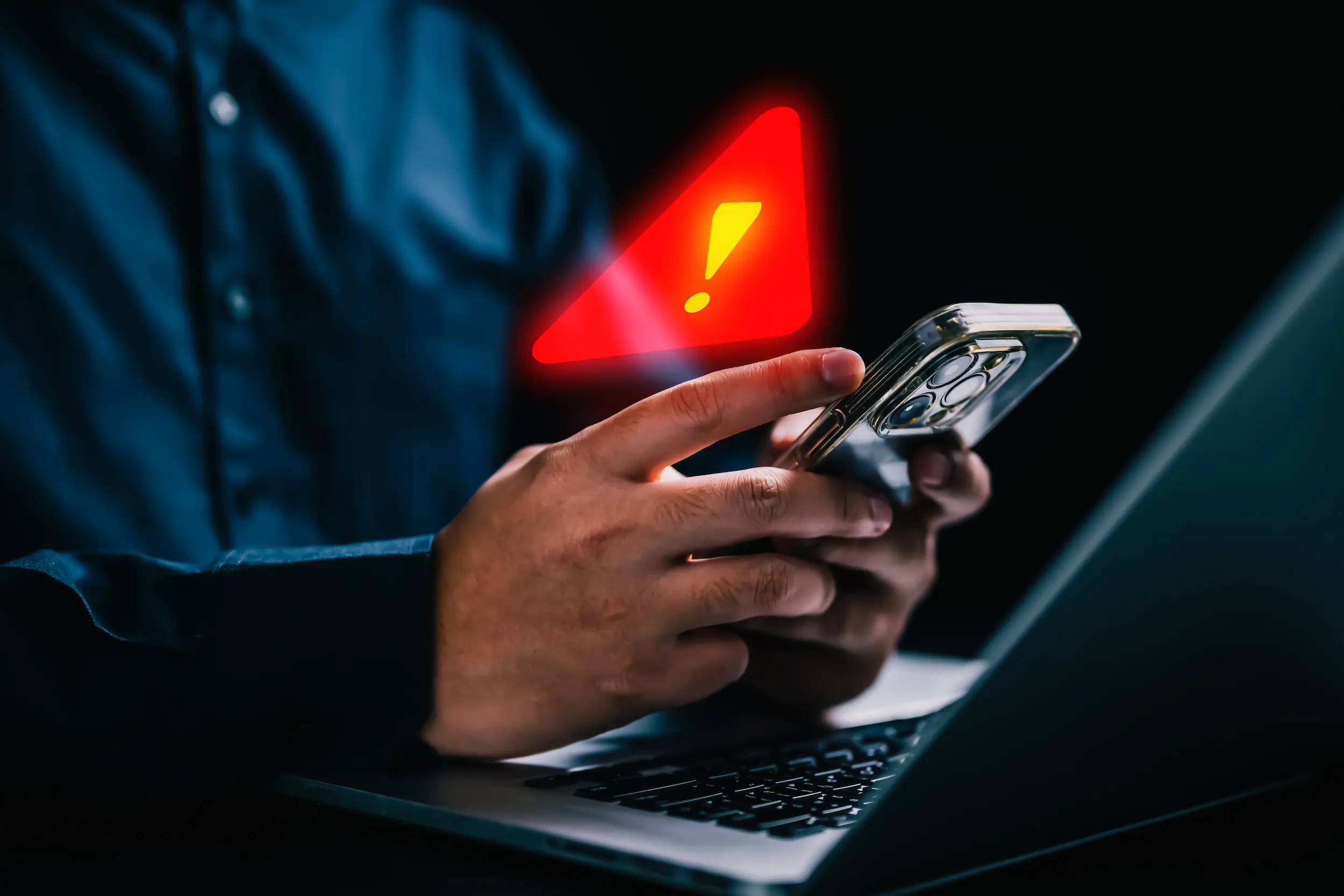 Pessoa usa celular com alerta de segurança digital ao lado de um notebook.