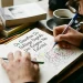 Pessoa escrevendo em um caderno com letras maiúsculas e minúsculas misturadas, explorando a expressão e a criatividade na escrita.