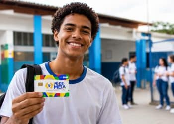Estudante do ensino médio público segurando cartão do Pé-de-Meia, programa que paga R$ 200 por mês a quem cumprir 80% de frequência escolar