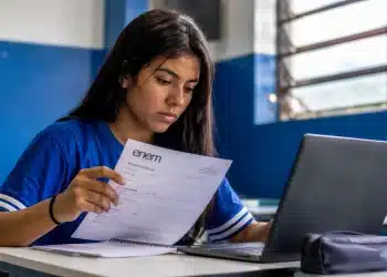 Estudante brasileira consultando documento de inscrição do Enem em frente ao notebook, representando o prazo de inscrição até 12 de junho.