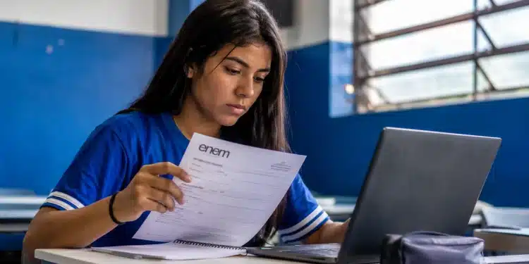 Estudante brasileira consultando documento de inscrição do Enem em frente ao notebook, representando o prazo de inscrição até 12 de junho.