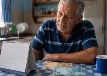 Aposentado brasileiro analisando calendário do INSS de junho com notas de R$100 e R$50 sobre a mesa, representando as três datas importantes de pagamento do mês