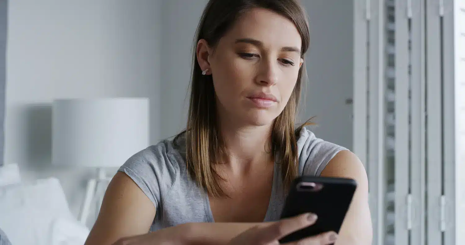 Mulher olhando para o celular com expressão neutra, representando a falta de disponibilidade imediata mesmo estando conectada.