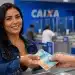 Mulher sorridente recebendo dinheiro na Caixa, representando o pagamento do lote extra do PIS/Pasep 2026.