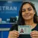 Jovem brasileira exibindo a carteira de habilitação no posto do Detran, representando o processo de matrícula na CNH Social em 2026.