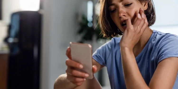Mulher utilizando smartphone e demonstrando preocupação ao responder mensagens enquanto permanece conectada nas redes sociais.