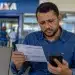 Trabalhador preocupado conferindo documento e celular em agência da Caixa, representando a liberação do benefício em 15 de junho e os motivos que podem bloquear o pagamento.
