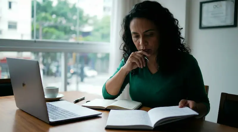 Mulher concentrada estudando com notebook e cadernos, simbolizando orientação para reconversão profissional.