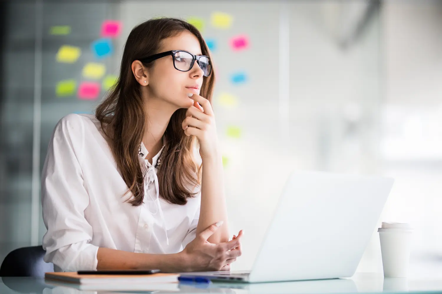 Mulher pensativa diante do notebook em ambiente corporativo, representando o planejamento de uma transição de carreira bem-sucedida.