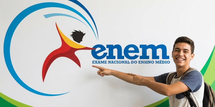 Jovem sorridente aponta para o logotipo do Enem fixado em parede branca