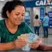 Mulher segurando cédulas em agência da Caixa, representando os pagamentos do Bolsa Família de junho de 2026, com liberação de até R$ 1.000.